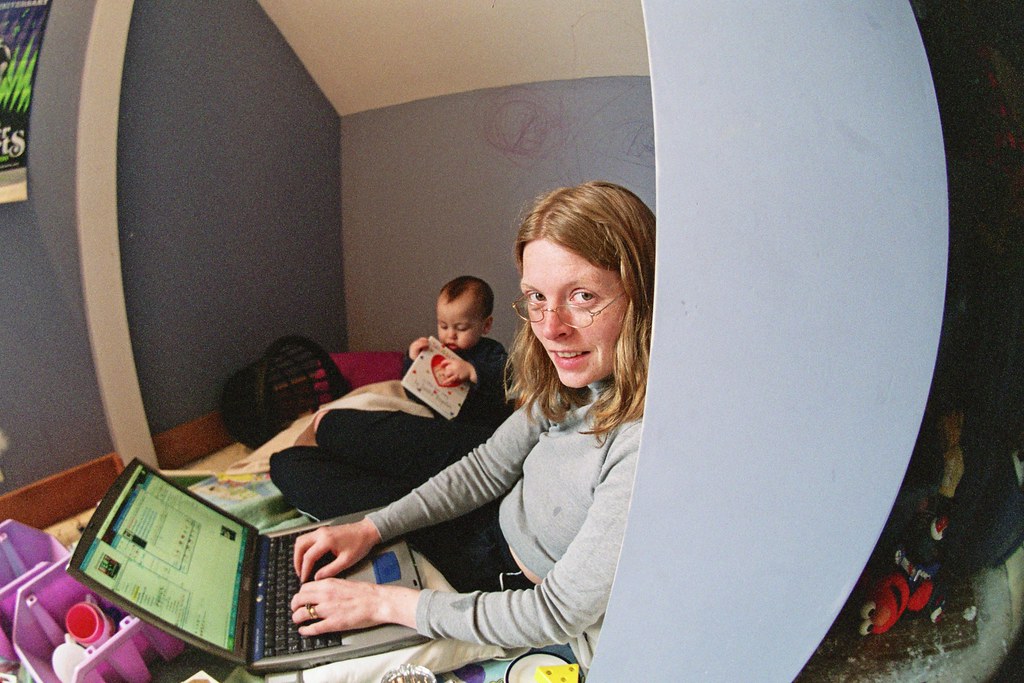 A woman working on her computer with a toddler nearby.